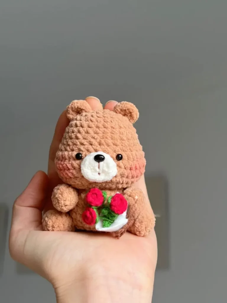 Small crocheted teddy bear holding flowers.