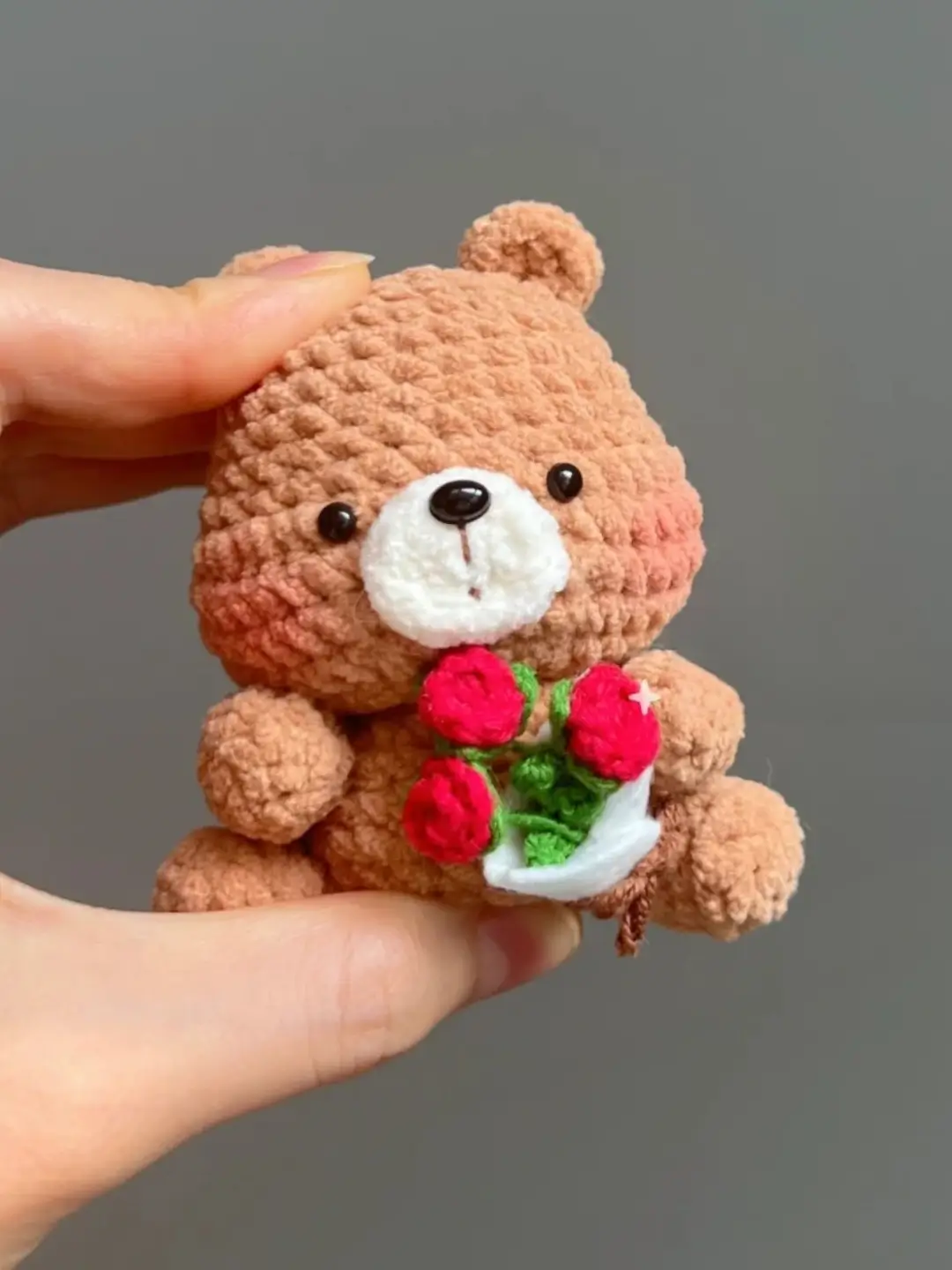 Cute crocheted teddy bear holding flowers.