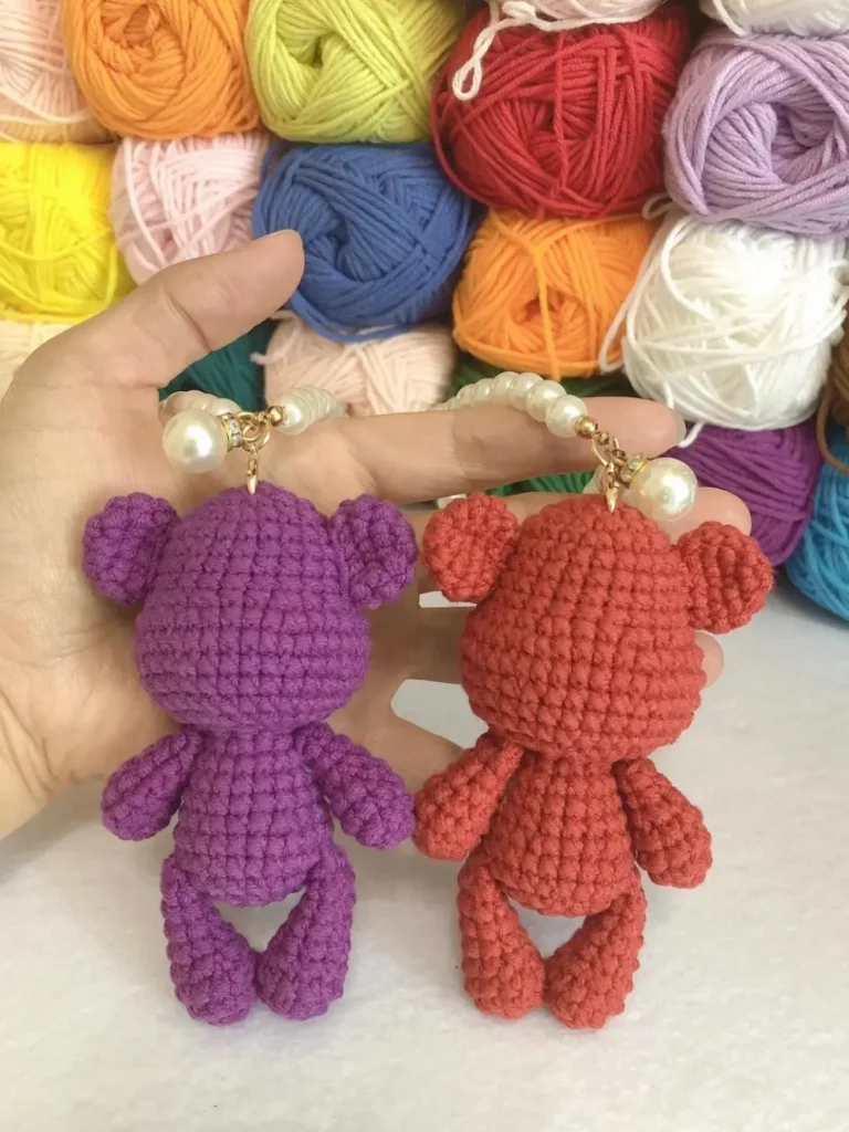 Two crocheted teddy bears, purple and orange, with pearl necklace.
