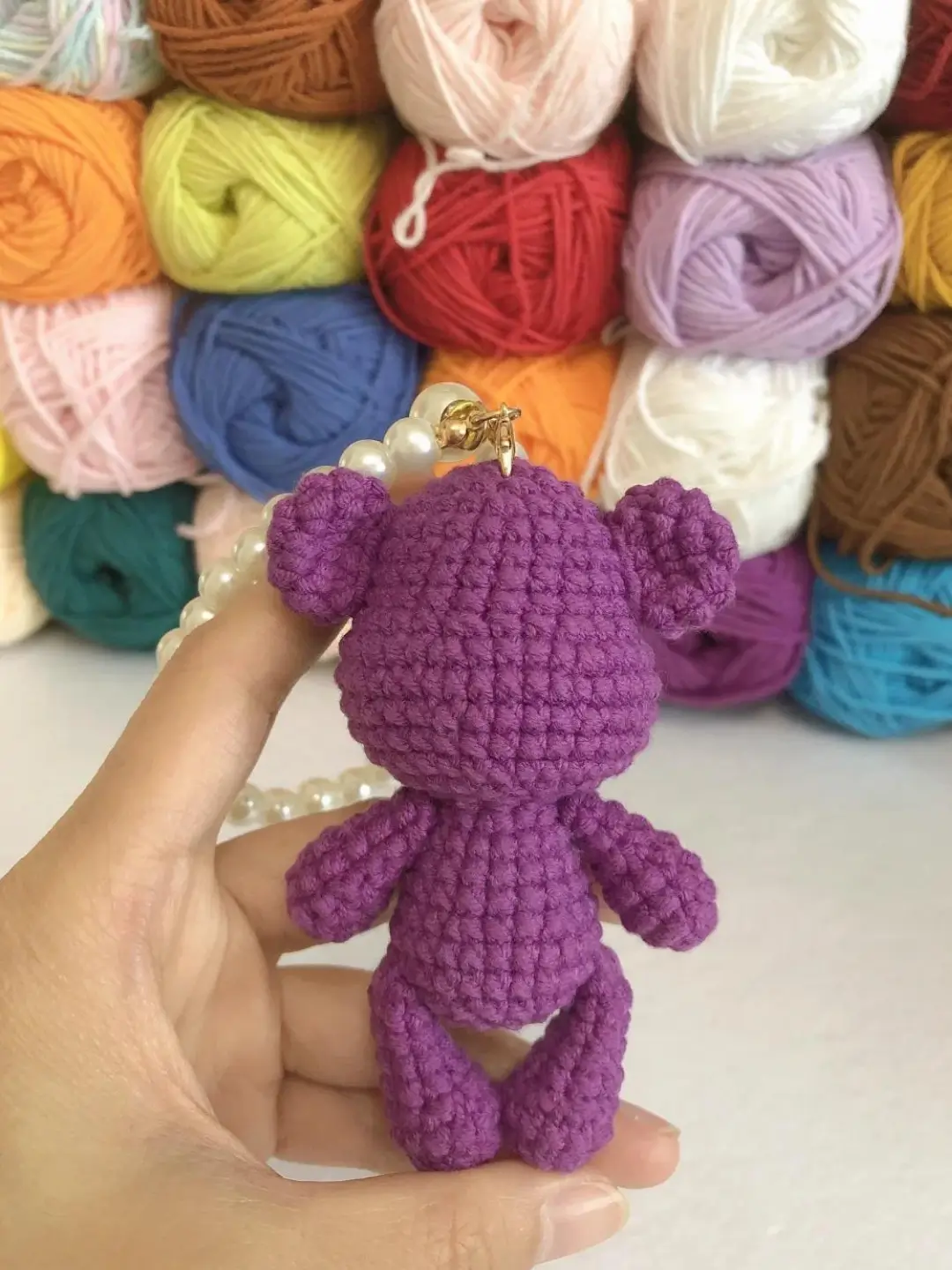 Crochet teddy bear, purple, yarn balls background.
