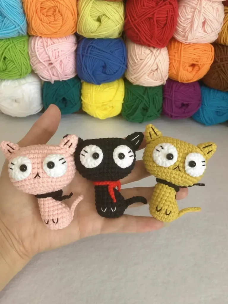 Crocheted cats, pink, black, yellow, yarn balls.