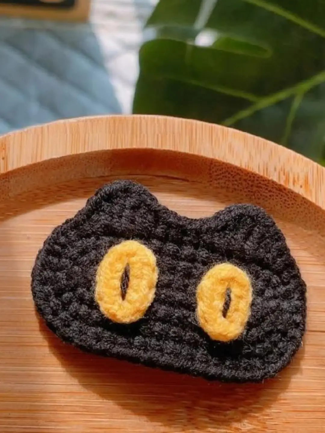 Crocheted black cat face, yellow eyes.