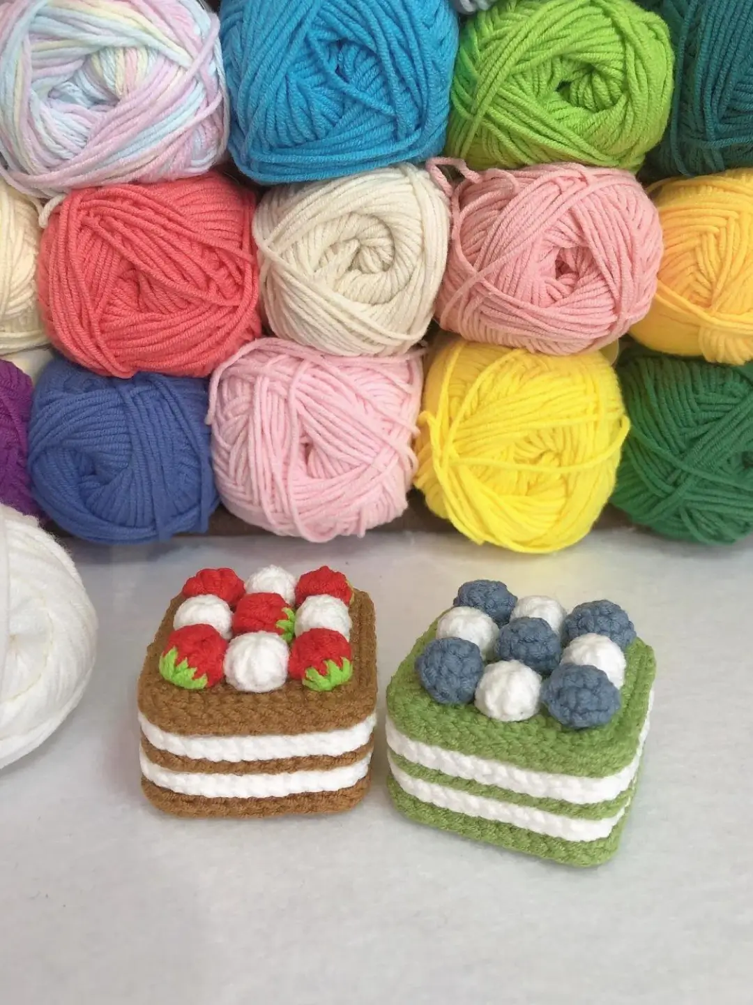 Crochet cakes, strawberry and blueberry, colorful yarn background.