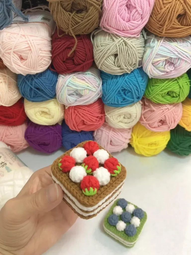 Crocheted strawberry and blueberry cakes, colorful yarn balls.