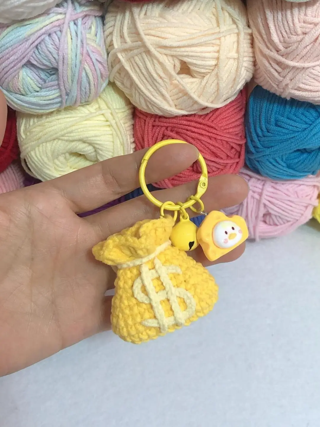 Crocheted yellow money bag keychain, colorful yarn balls background.