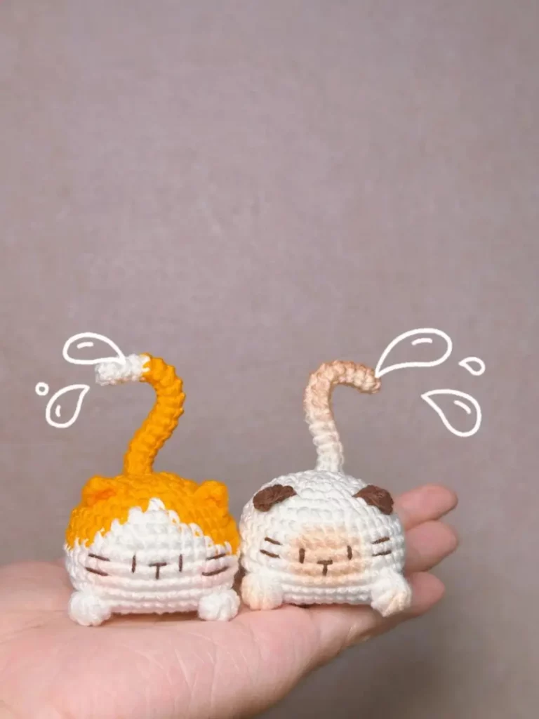 Two crocheted amigurumi cats, one orange and one beige, held in a hand.