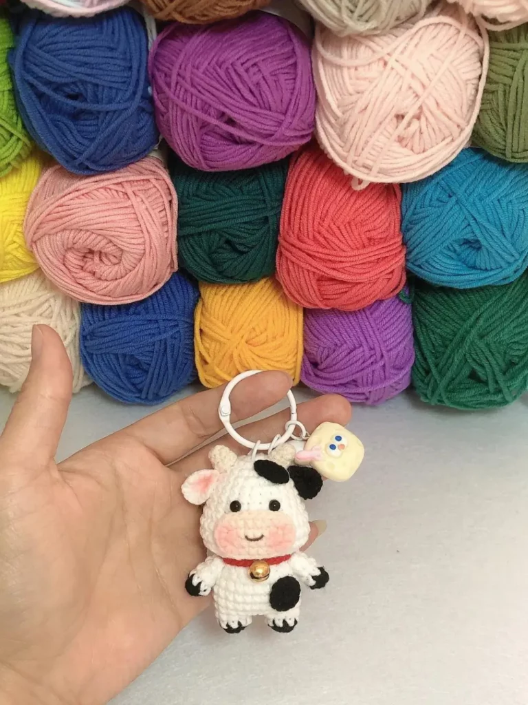 Crochet cow keychain, colorful yarn balls background.