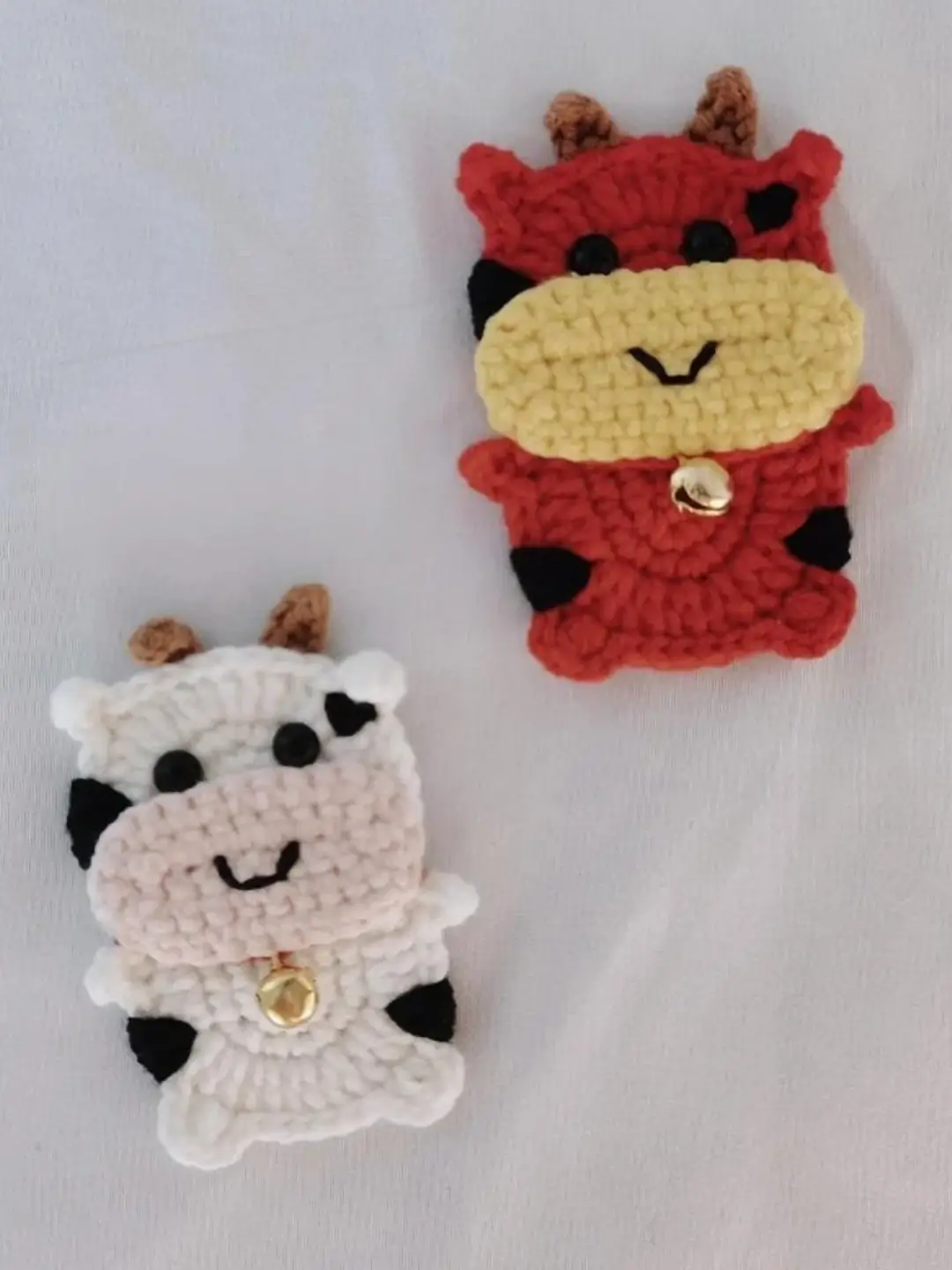 Two crocheted cow figurines, one red and one white.