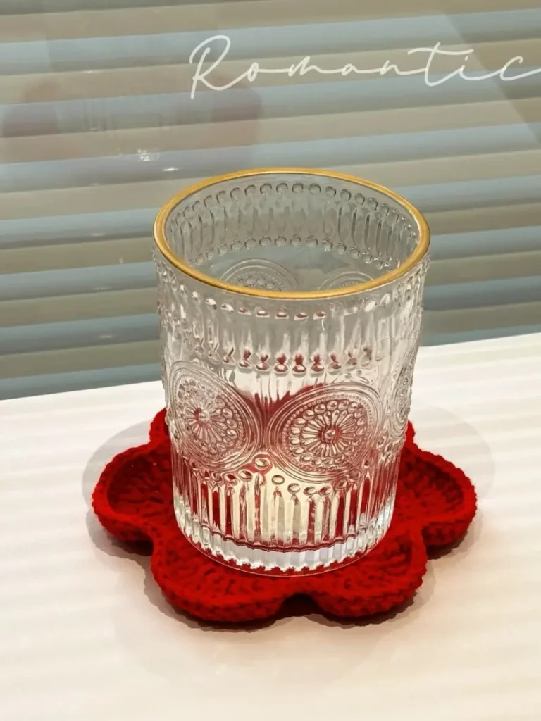 Clear glass tumbler with gold rim, on a red crocheted coaster.