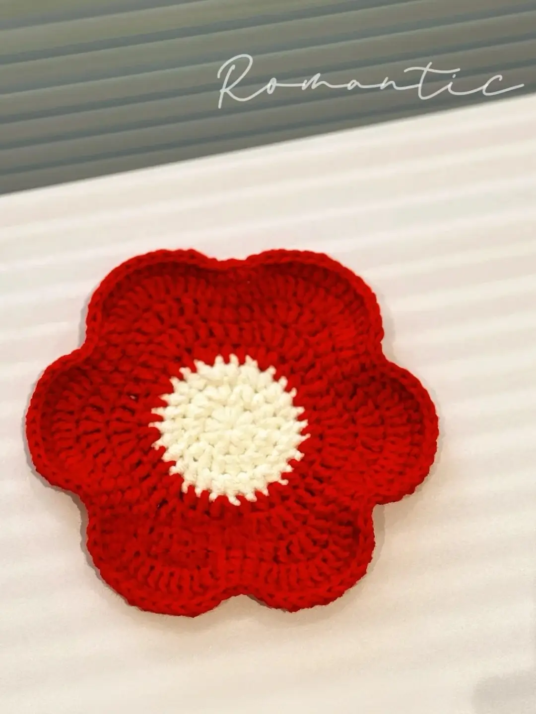 Crocheted red flower coaster with white center.