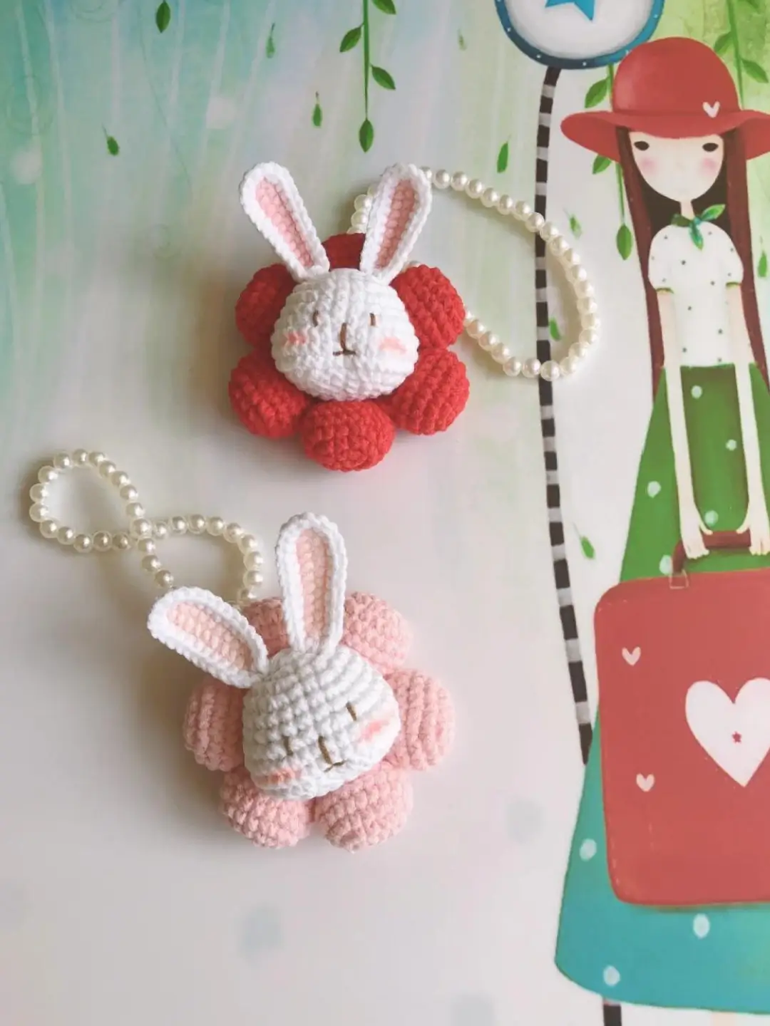 Two crocheted rabbit charms, red and pink, on pearl necklaces.