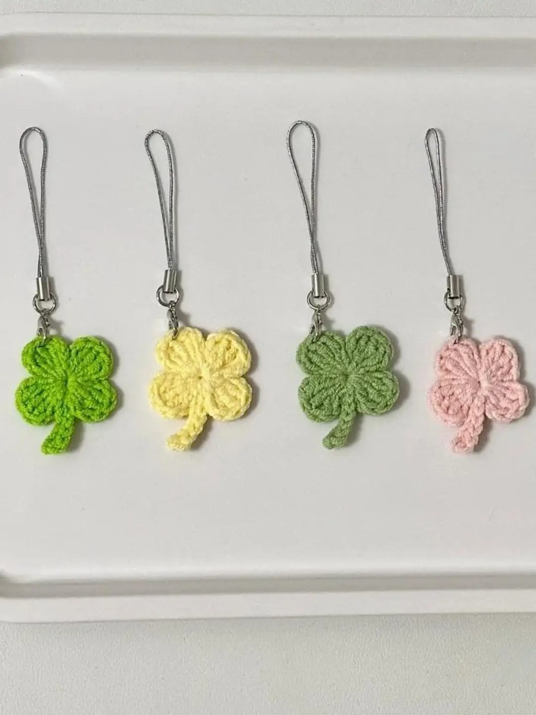 Four crocheted clover keychains in green, yellow, light green, and light pink.