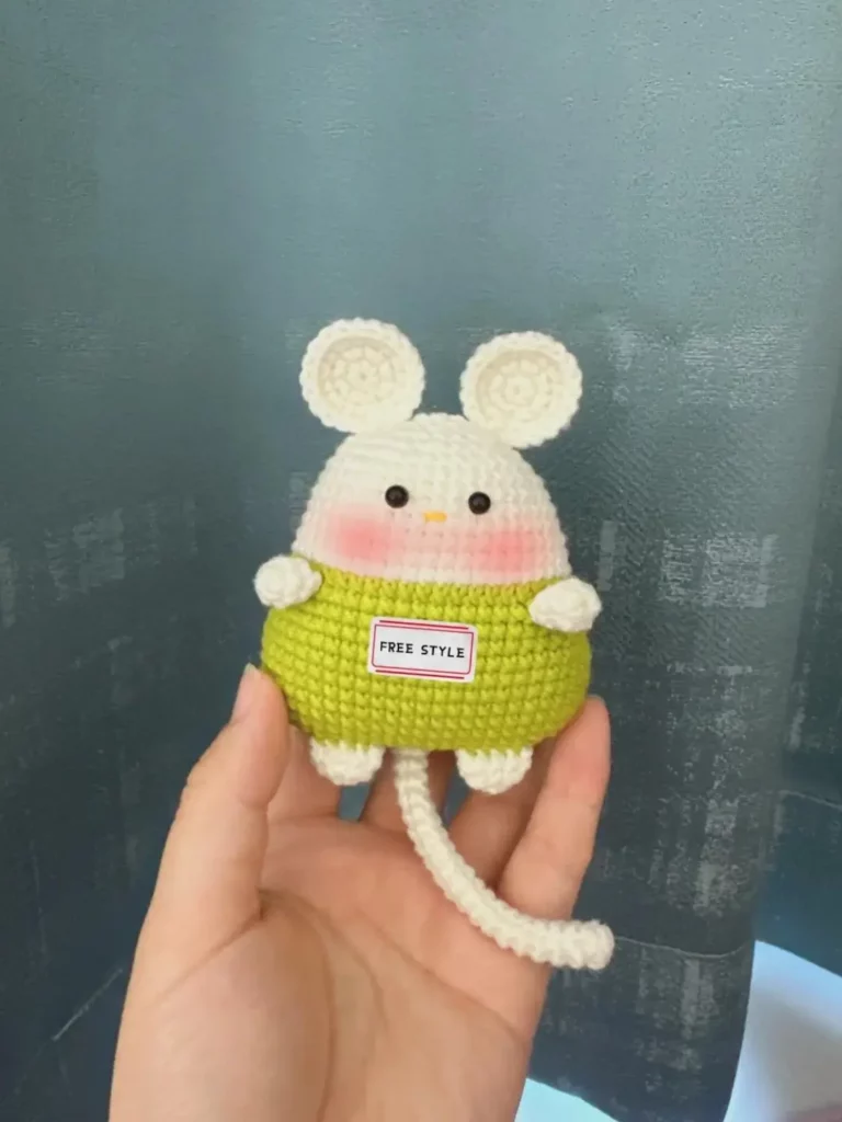 Crocheted mouse toy, light green, white ears, pink cheeks.