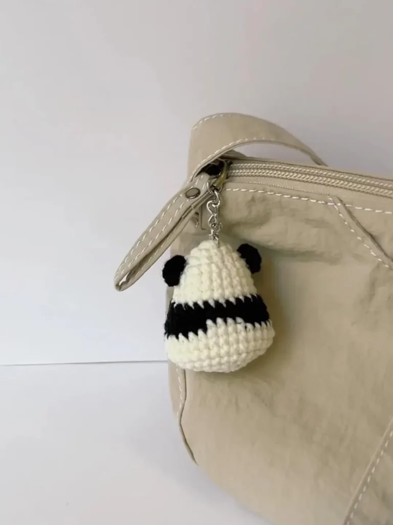 Crocheted panda keychain on beige bag.