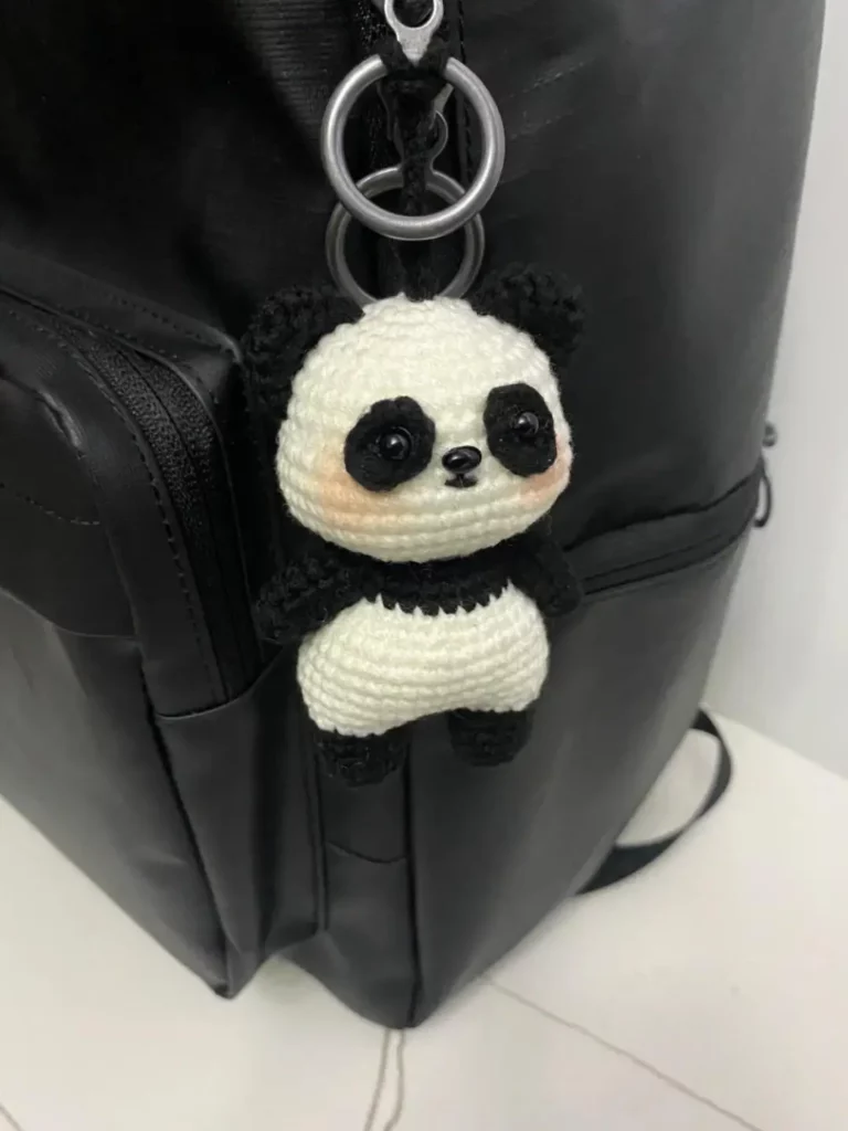 Crocheted panda keychain on black backpack.