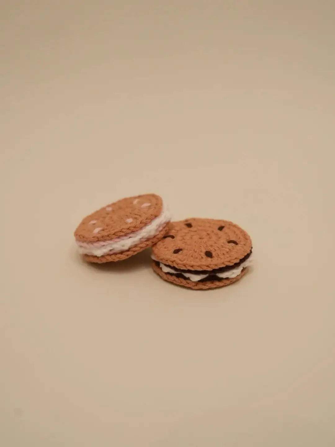 Two crocheted sandwich cookies, one with pink, one with chocolate filling.