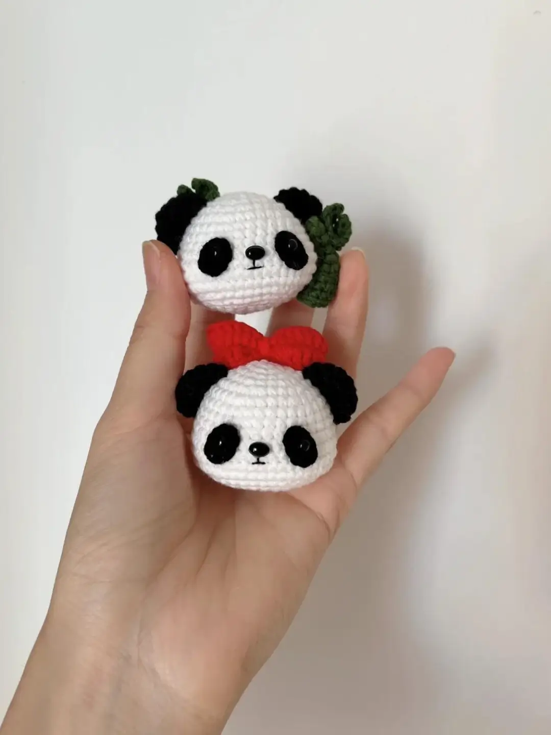 Two small crocheted panda heads, white with black features,  one with a red bow.