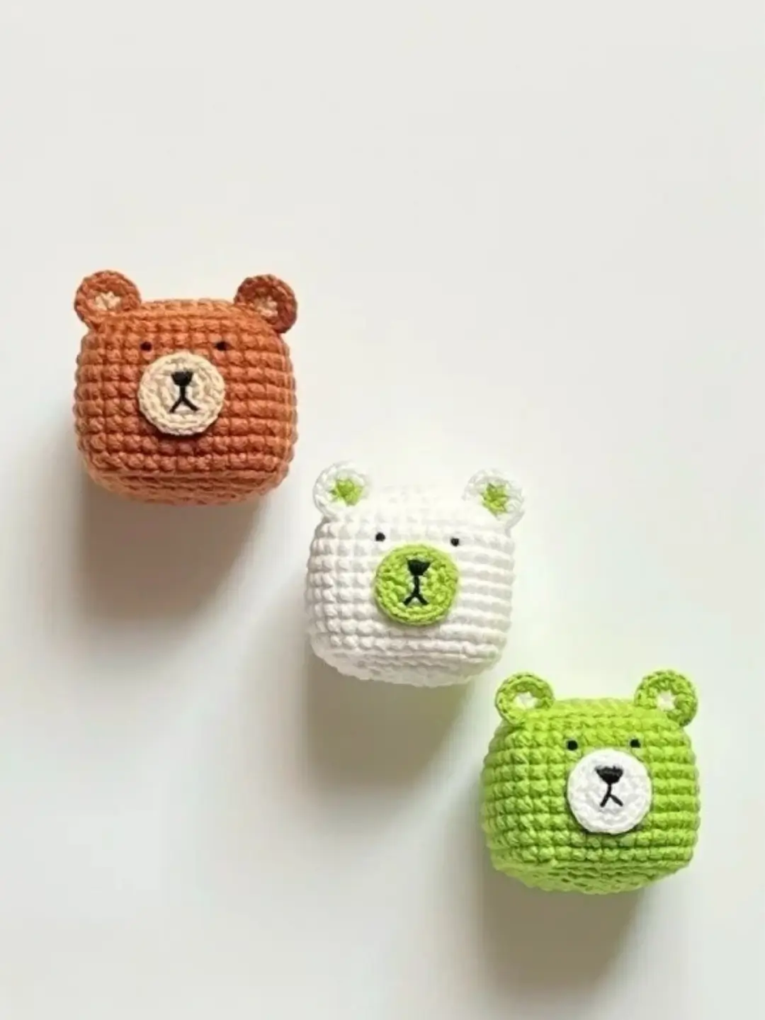 Three crocheted bear faces, brown, white, and green.
