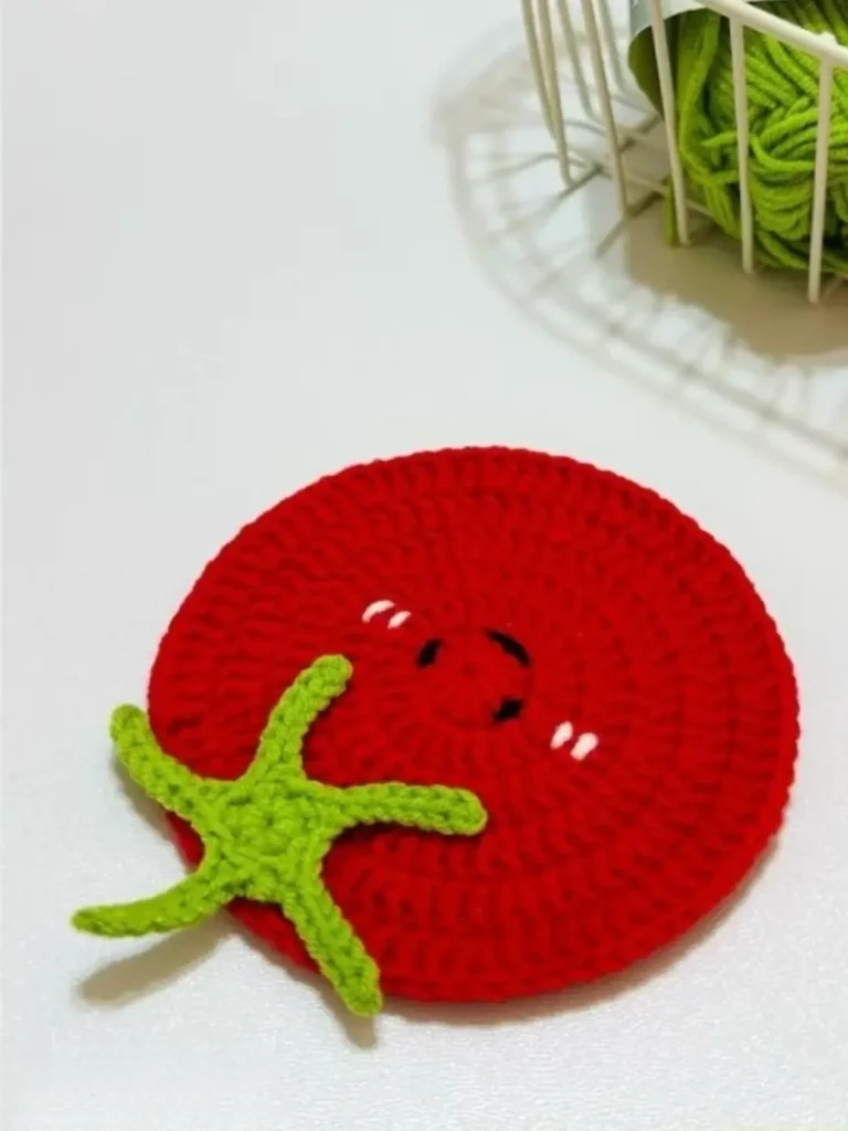 Crocheted tomato coaster, red with green stem.