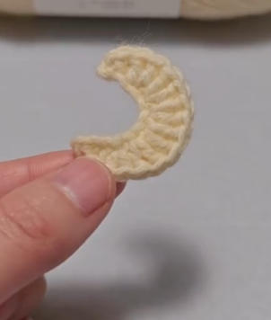 Crochet crescent, cream colored, held in hand.  Yarn craft.